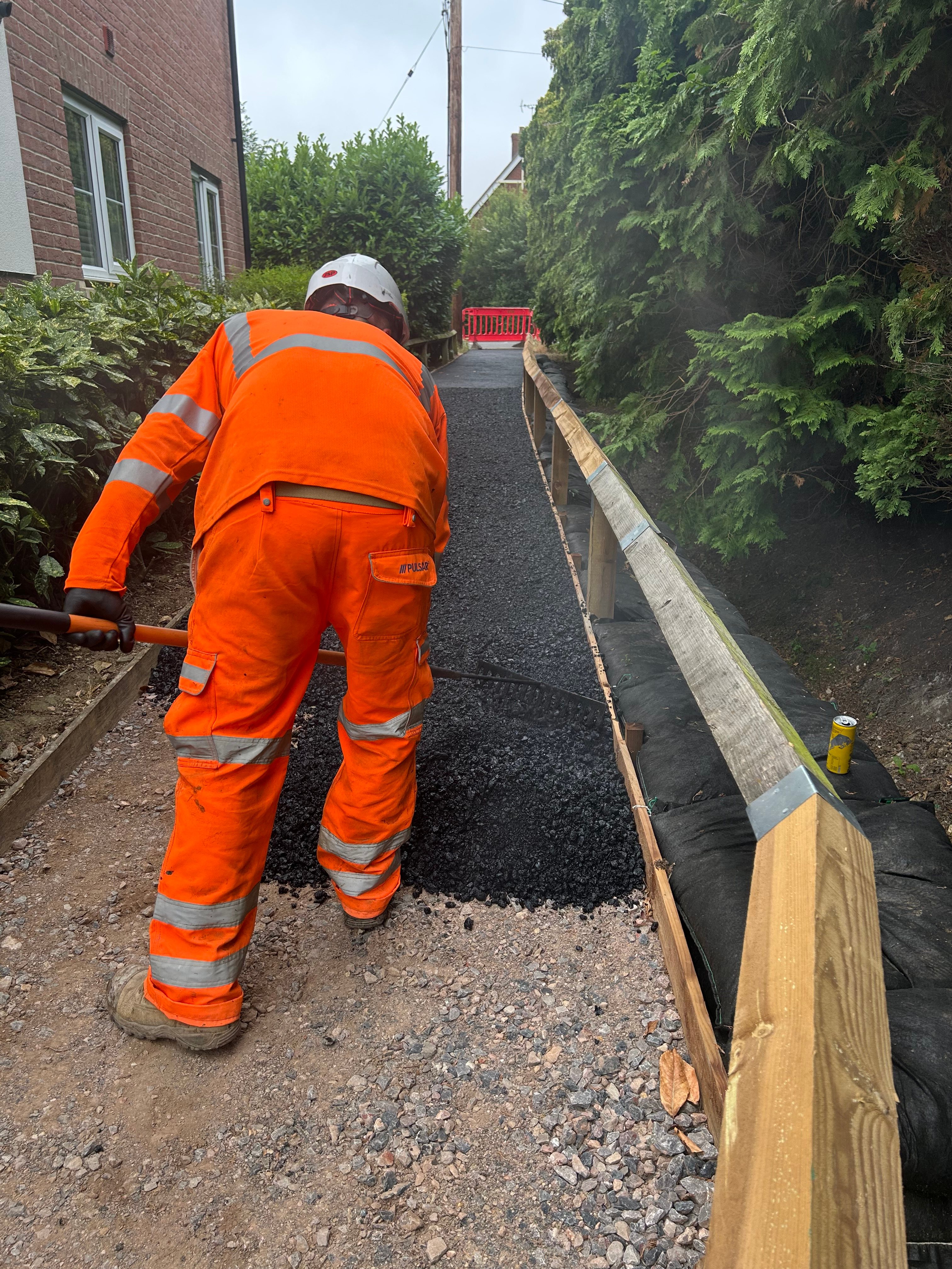 Worker laying fresh tarmac during footway resurfacing